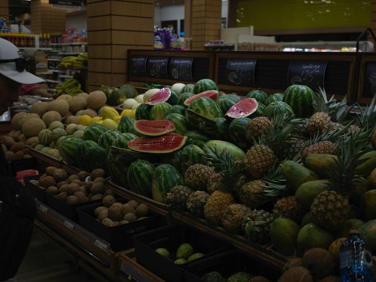 Woman holding a Tops flyer while smiling near fresh produce.