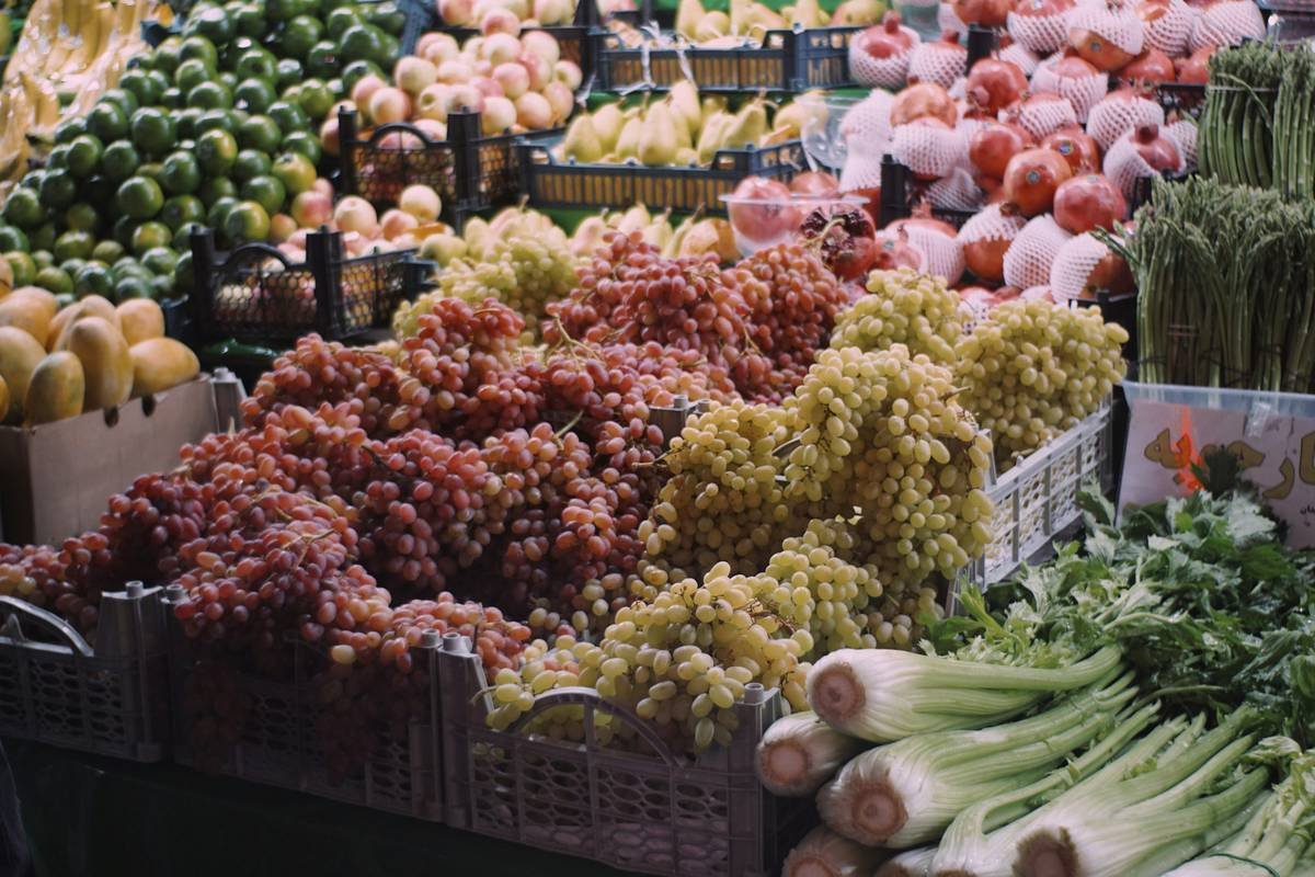 A person holding a reusable bag filled with fresh vegetables near checkout counters.
