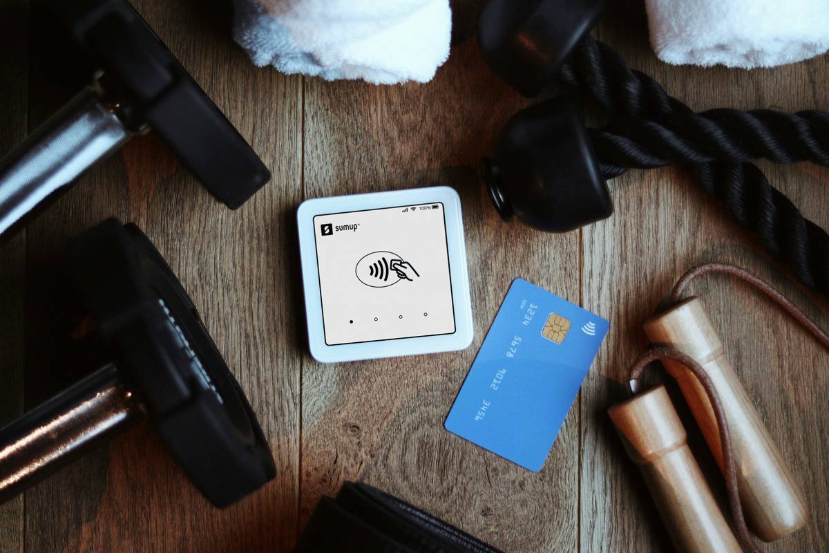 A SumUp Solo card reader placed on a wooden gym floor next to a blue credit card, a jump rope, and other fitness equipment. This image represents the ease of cashless payments in gyms, fitness studios, and wellness centers, allowing small businesses to offer a seamless and modern checkout experience.