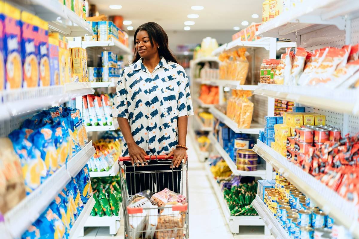 A shopper comparing prices at Tops Friendly Markets with a notebook titled 'budget effect on share market'